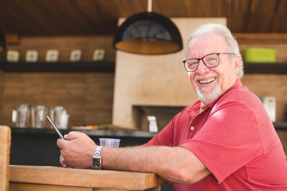 Someone sitting at a table is holding a smartphone and smiling.