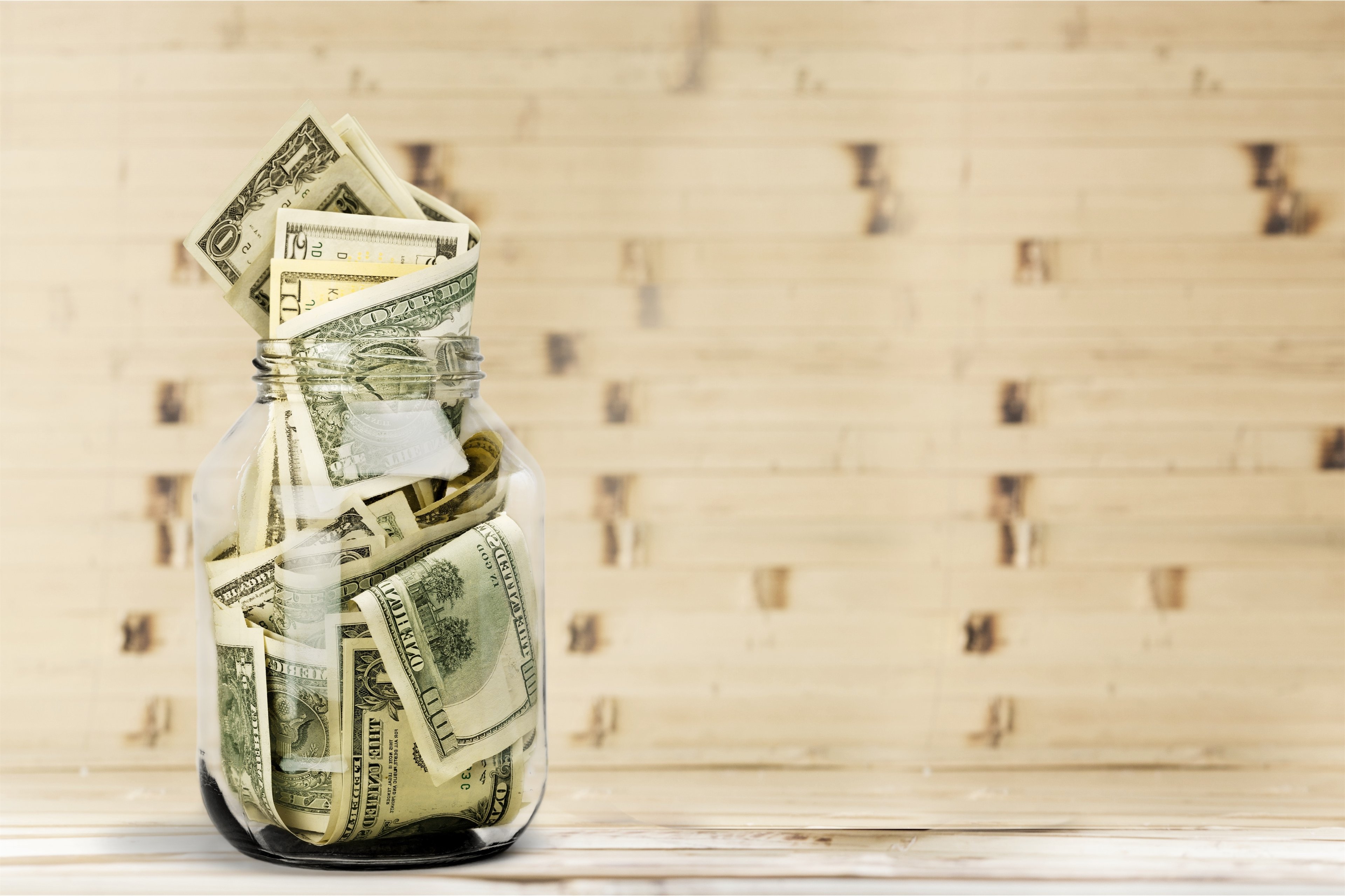 A jar of $100 bills on a wooden table.