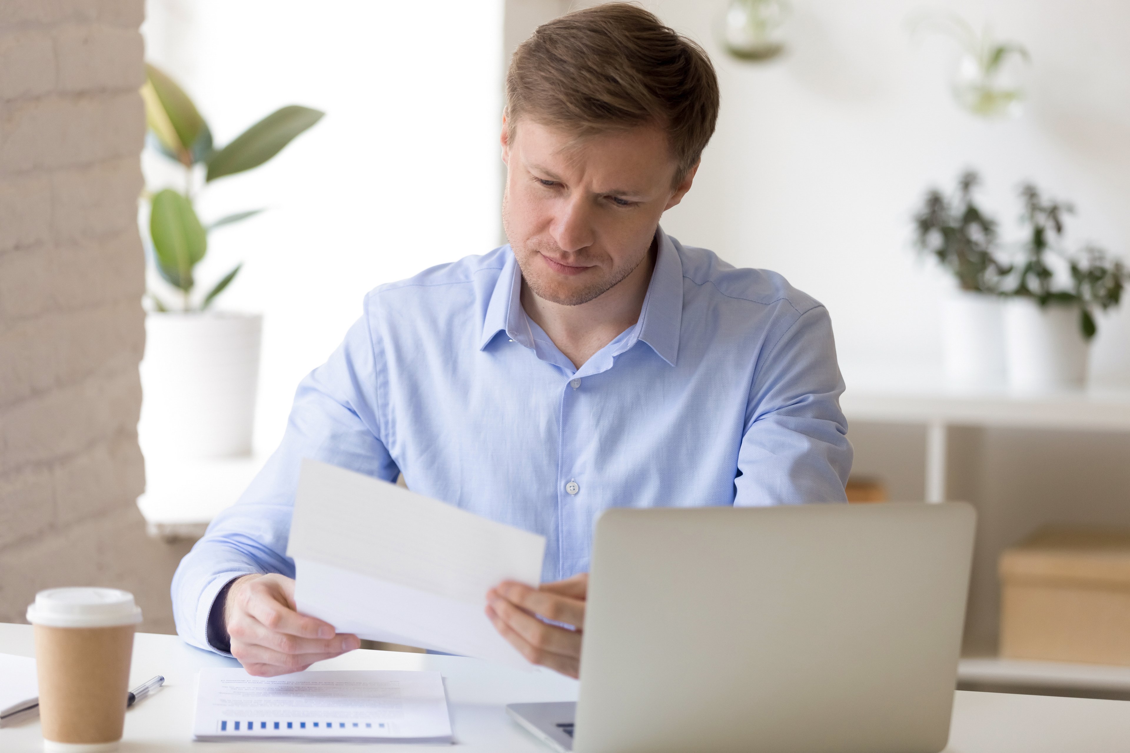 A person at a laptop holding a document.