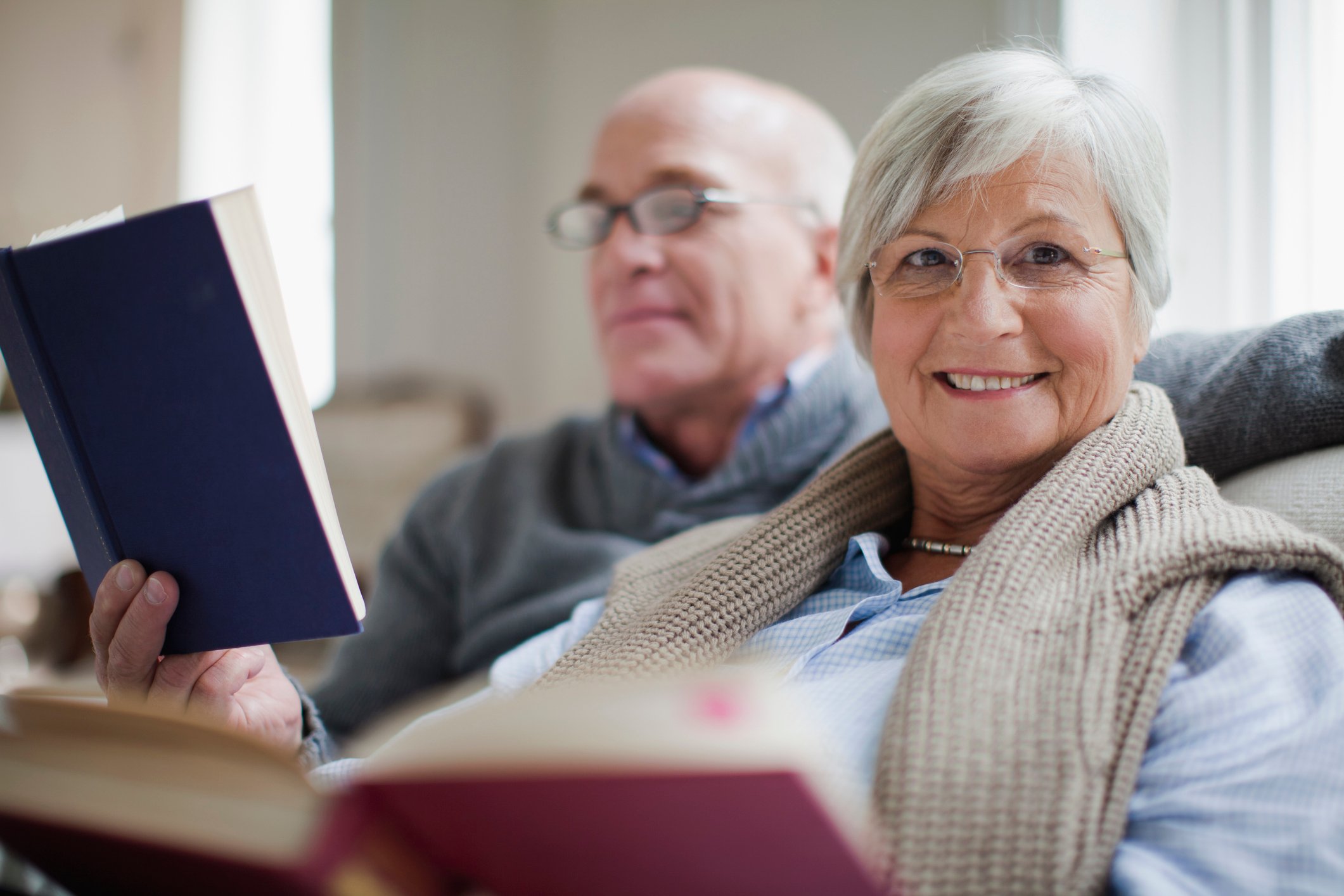 Two people on a couch, each reading a book and smiling.