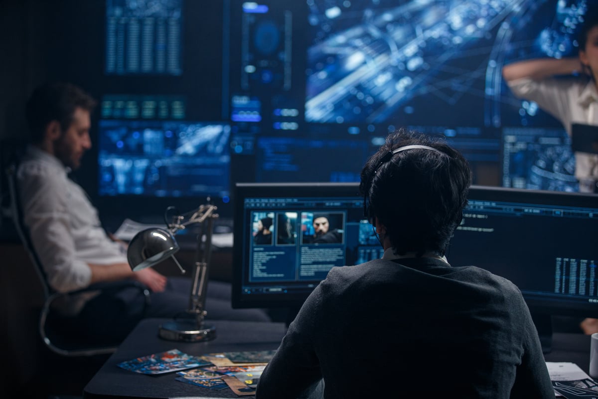 A team of data analysts collecting and analyzing data on a number of screens in a control room.