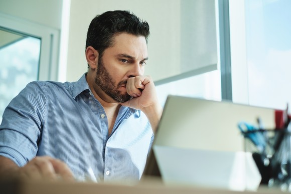 A person clinching their first and looking at a tablet computer on a table in a concerned manner. 