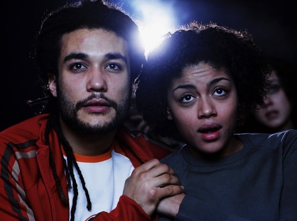 A couple at the movies clutching hands as the projector plays.