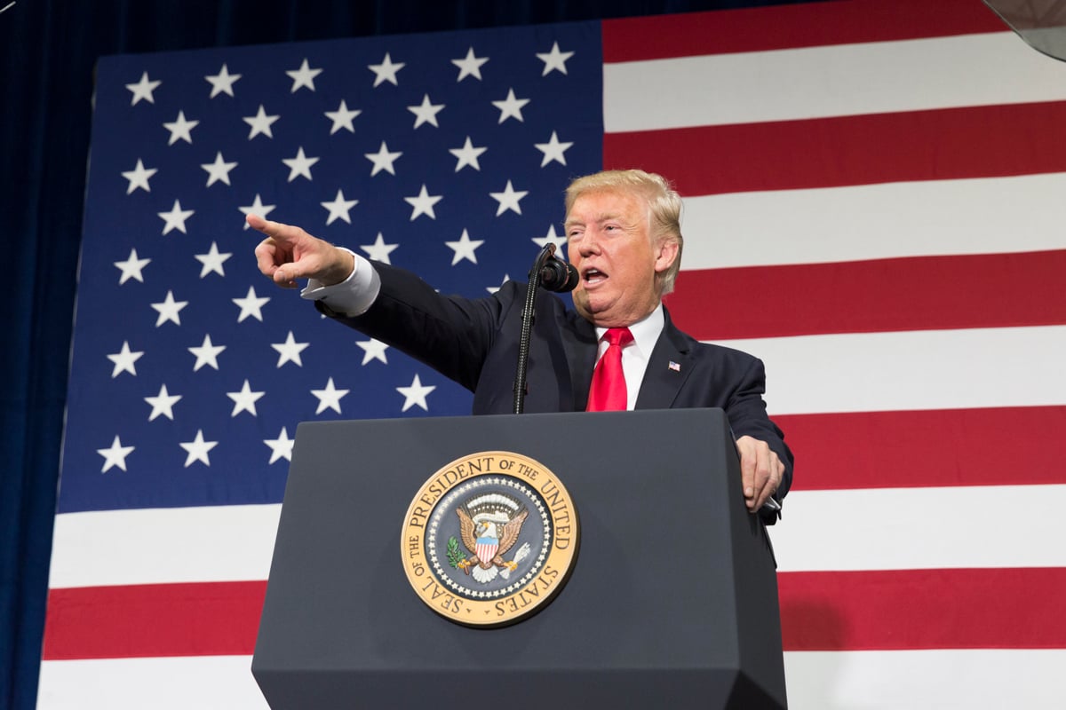 Former President Donald Trump giving remarks while standing in front of a large American flag.