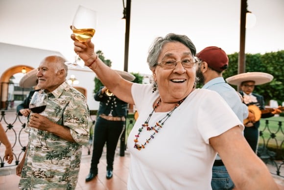 Someone is outdoors, dancing and smiling while holding a glass of wine. 