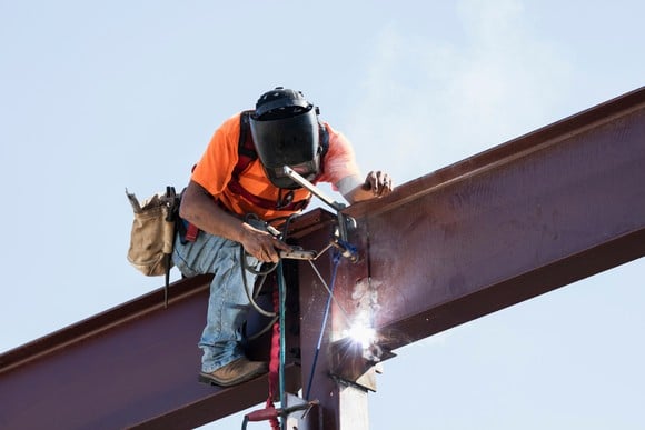 A welder wearing personal protective equipment works on a steel girder. 