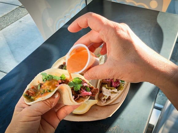 A hand pours sauce over food wrapped in a tortilla.