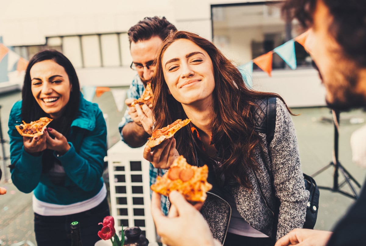 Group of people with vibrant facial expressions holding a slice of pizza in their hands.