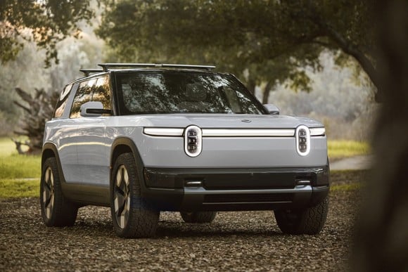 A gray prototype Rivian R2, a midsize electric SUV that the company expects to launch in mid-2026, parked under a tree in a rural setting.