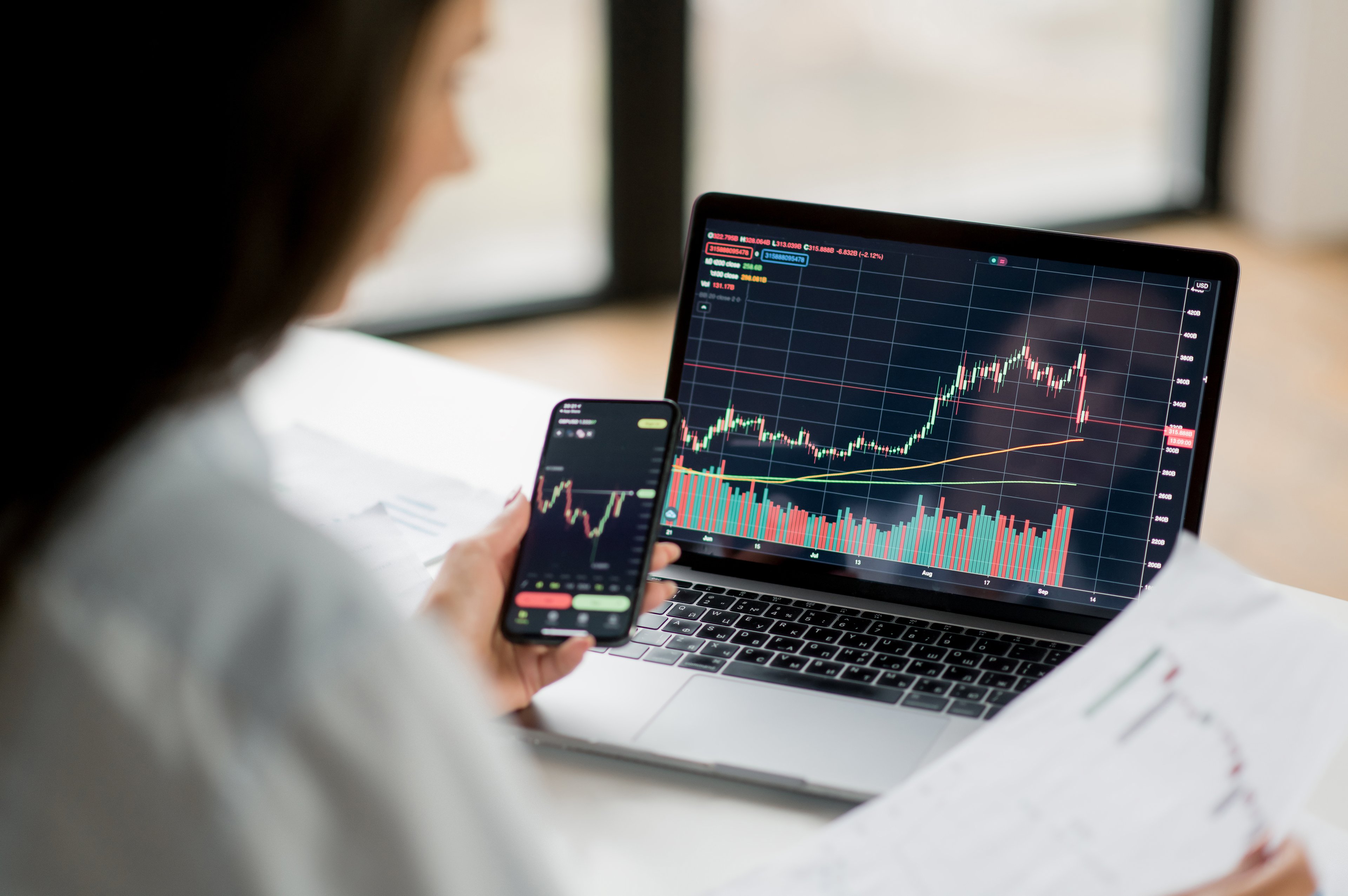 person looks at stock chart on phone and computer