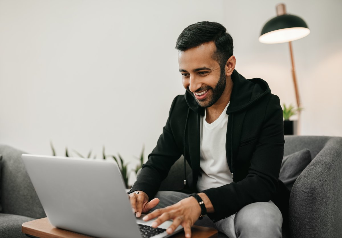 A person smiles while sitting on a chair and typing on a laptop computer. 