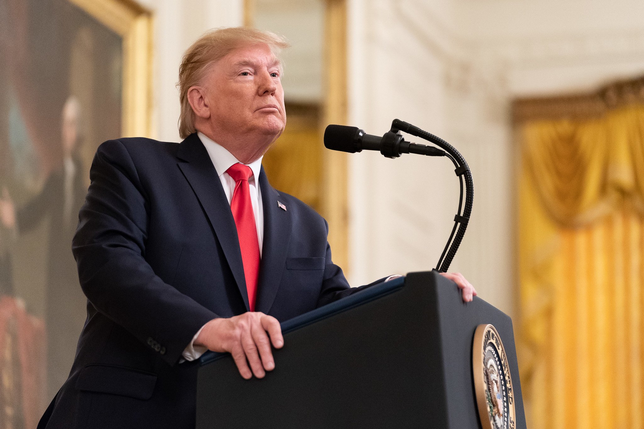 Donald Trump delivering remarks behind the presidential podium while in the East Room of the White House.