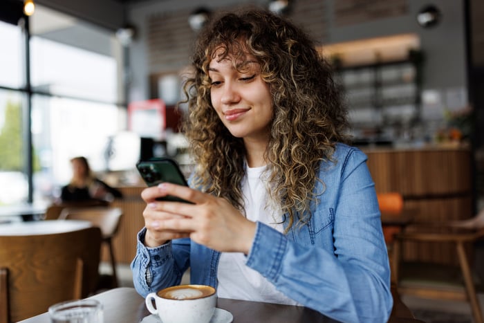 A person sitting in a restaurant on their phone with an espresso drink on the table. 