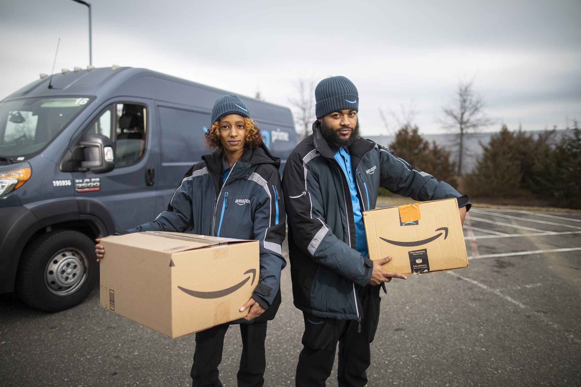 Two Amazon delivery drivers carrying cardboard boxes with the company's logo.