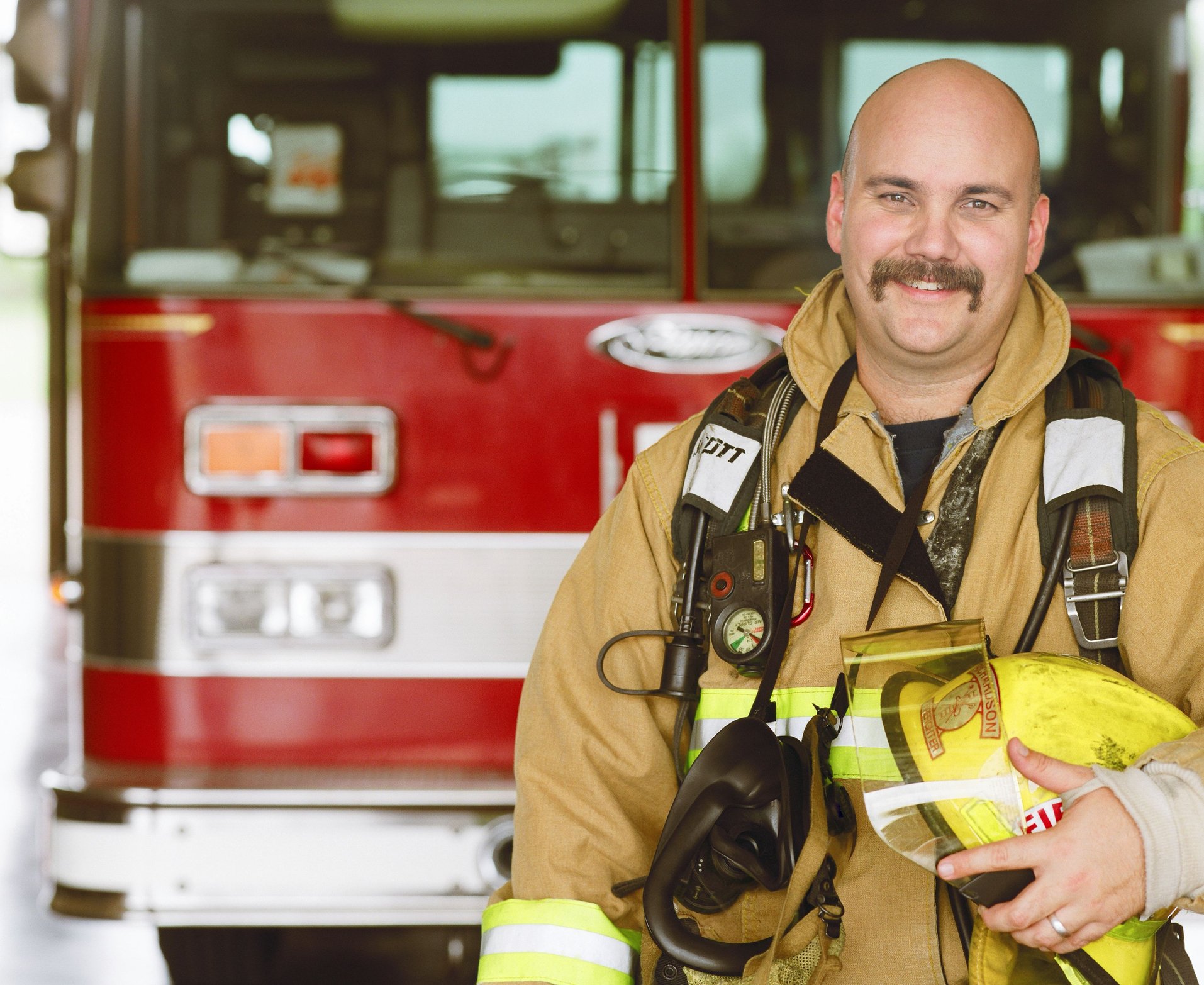A firefighter is smiling in front of a fire truck.