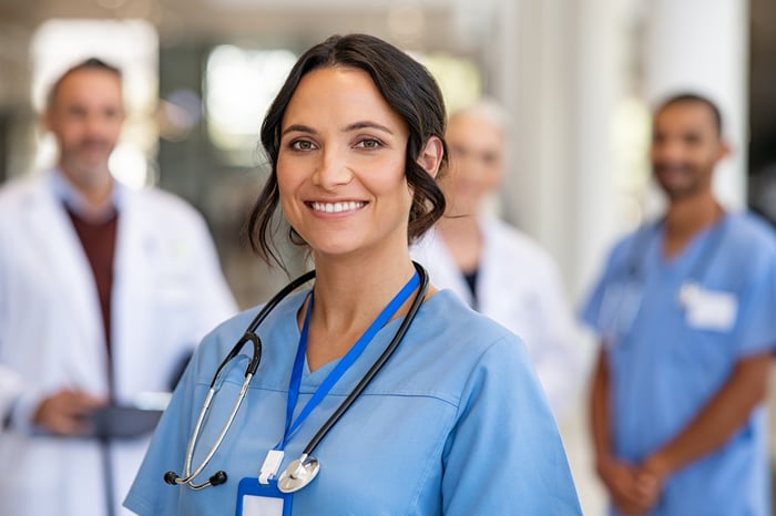 A smiling healthcare worker in front of other healthcare workers.