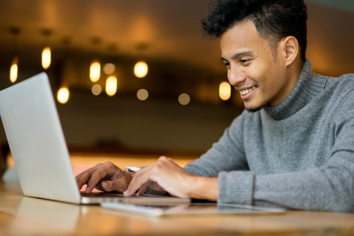 A person typing on a laptop while seated inside of a cafe.