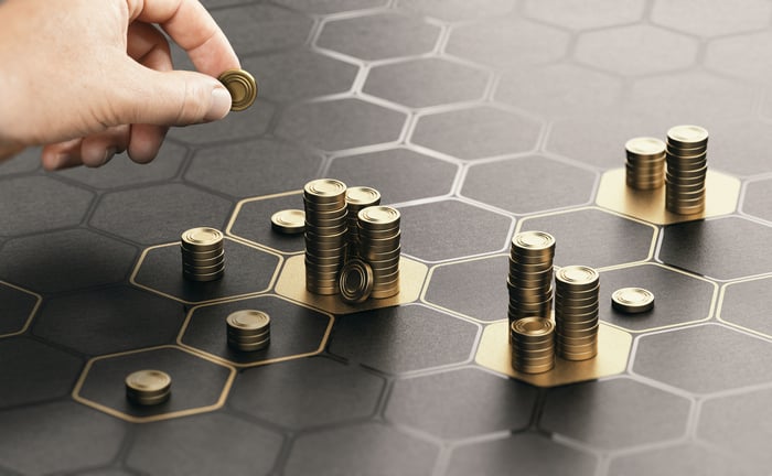 A person stacking gold coins into towers on top of gold and grey hexagons. 