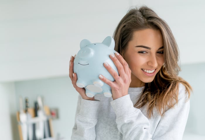 Smiling person shaking a piggy bank.