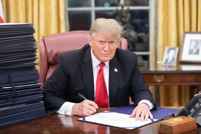 Donald Trump signing paperwork while seated at a desk in the Oval Office.