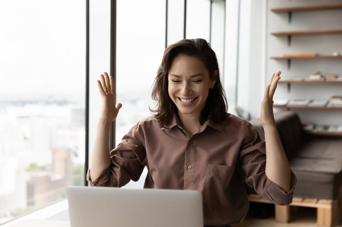 An investor cheers in front of a laptop in an office.