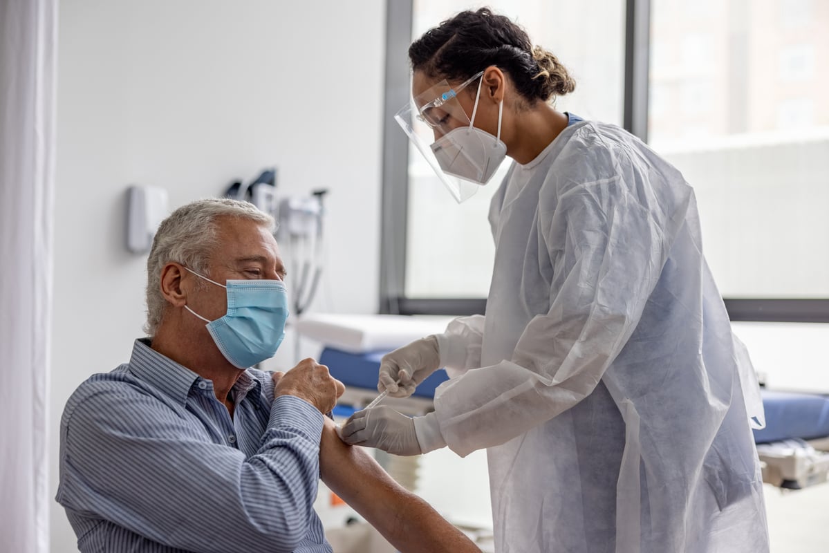 A healthcare professional in full personal protective equipment administers an injection to a patient.