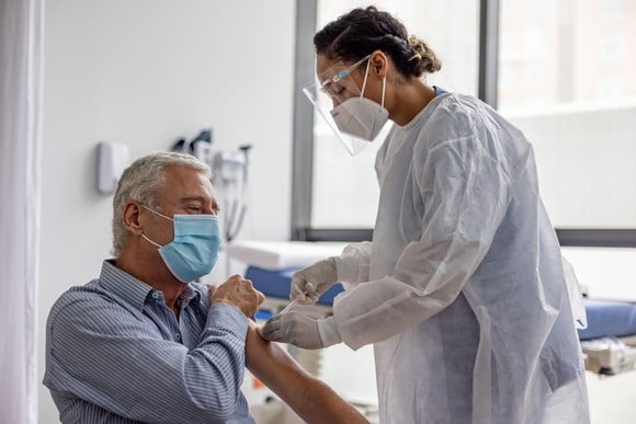A healthcare professional in full personal protective equipment administers an injection to a patient.