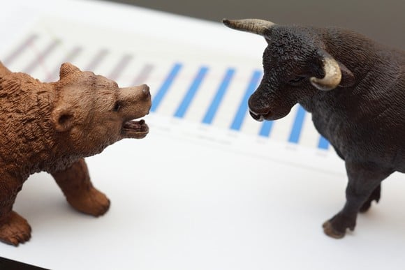 Bull and bear figurines facing one another on top of a print out of a bar graph.