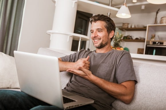 Someone is smiling at an open laptop and signing. 
