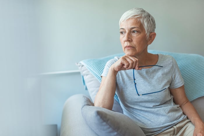 Worried person holding glasses and looking off into the distance.