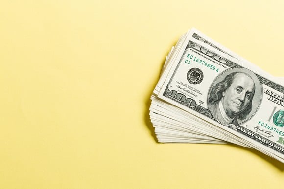 Stack of hundred-dollar bills against a yellow backdrop.