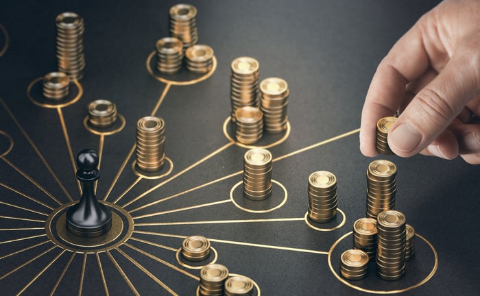 A person stacking gold coins into towers that are within gold circles emitting from a black pawn chess piece.