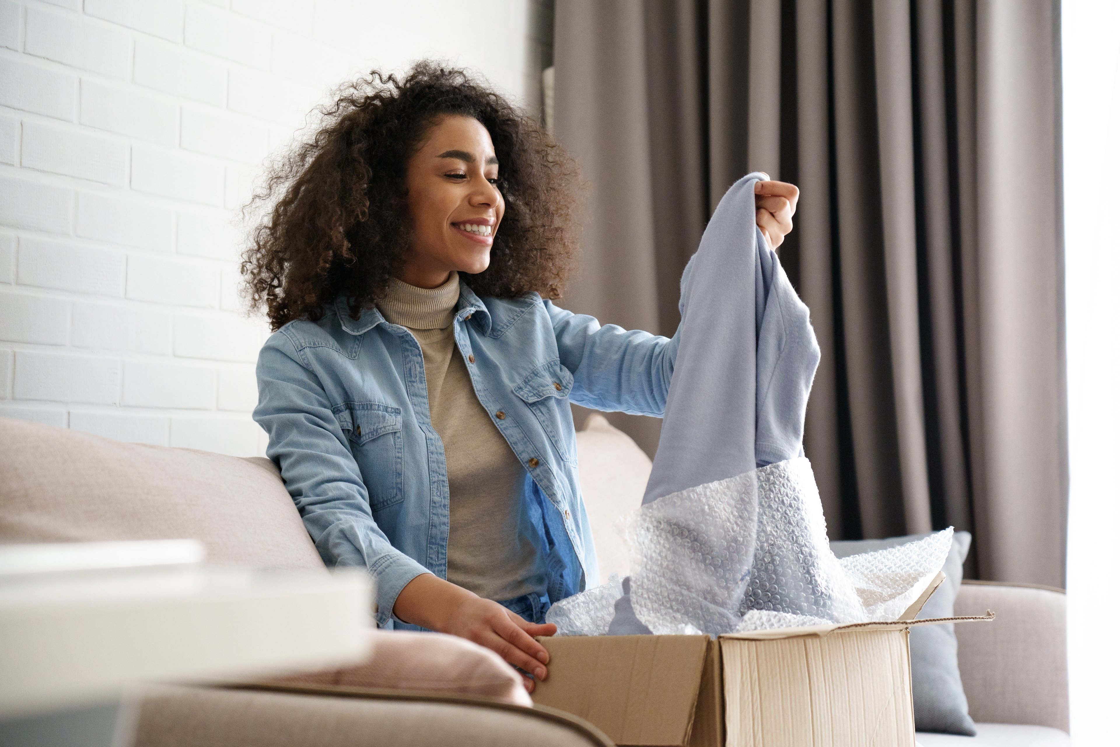 A person pulls a sweater out of a package in a living room.