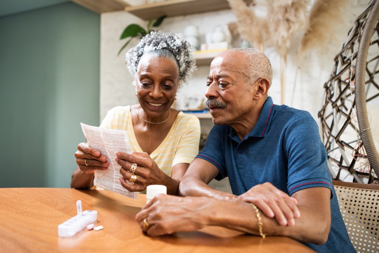 Couple sitting at table with medications and looking at document.