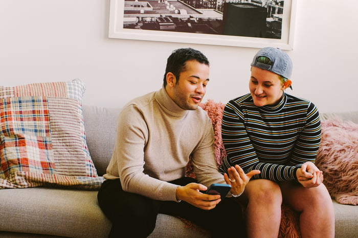 Smiling couple discussing something on smartphone.