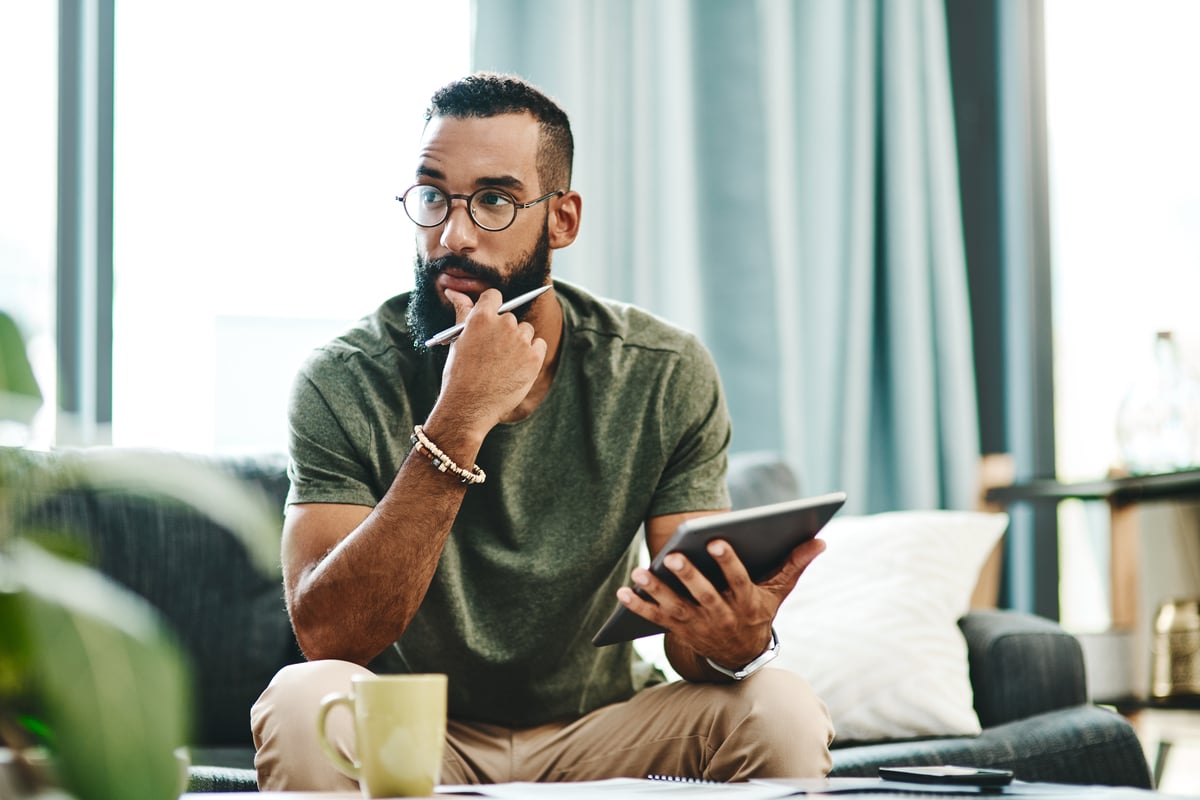 A person holding a stylus and a tablet while sitting on a couch. 