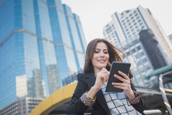 An investor looks at something on a tablet while standing on a city street.