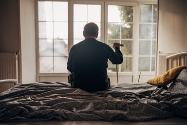 retired man with cane sitting on bed