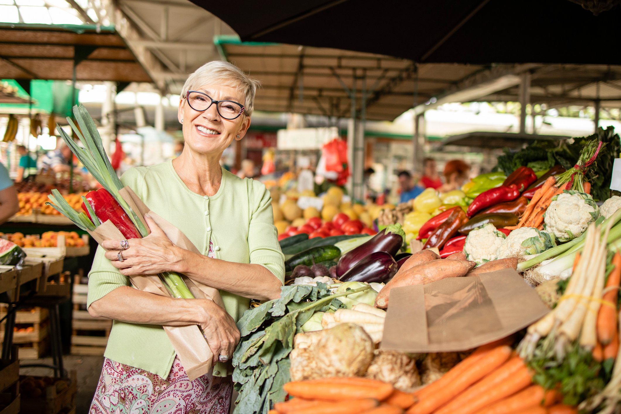 A person at a produce market holding veggies and smiling.