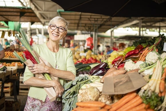 A person at a produce market holding veggies and smiling.