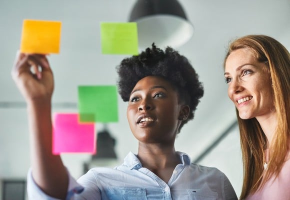 Two people smile while writing on sticky notes. 