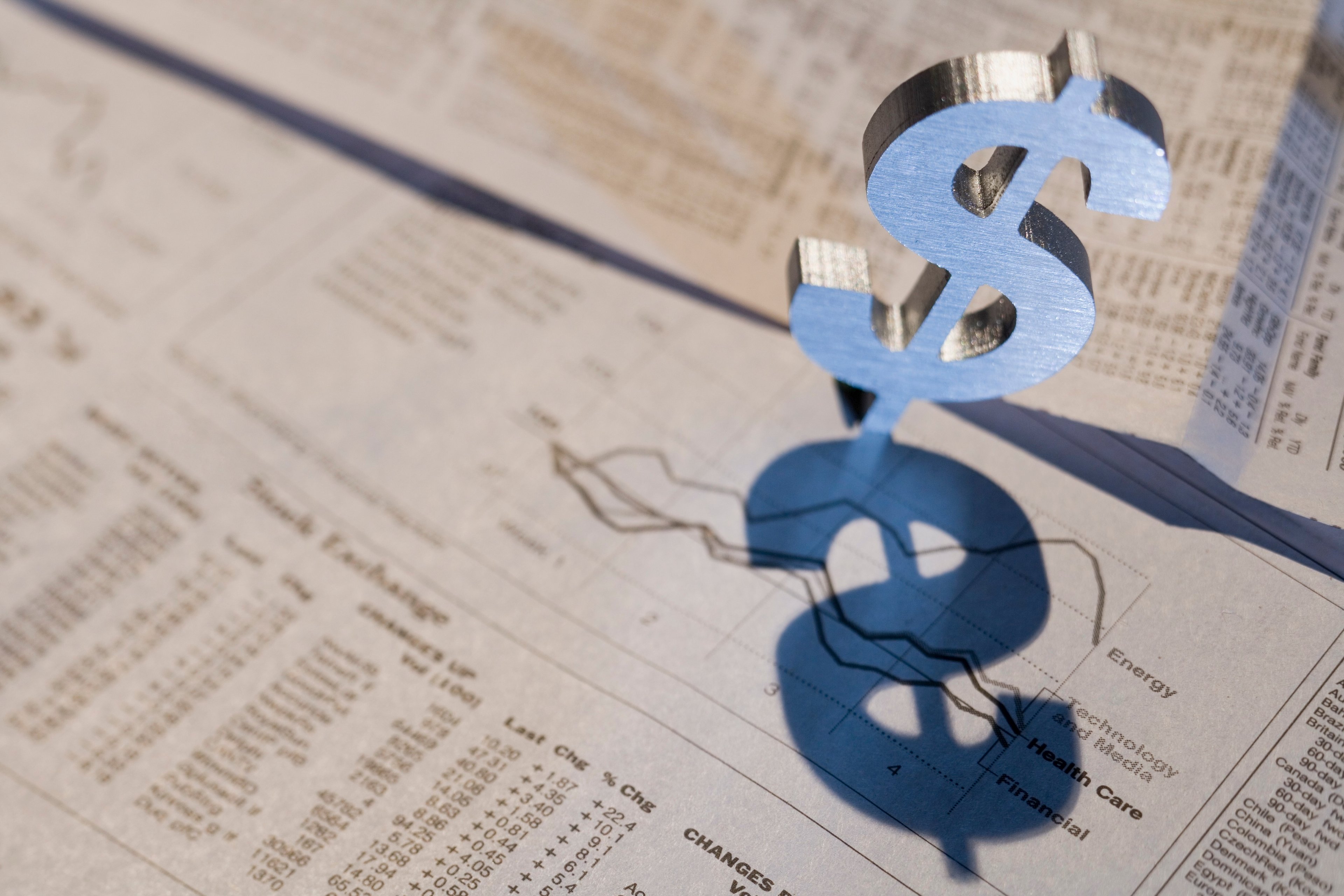 A metal dollar sign standing over a newspaper show stock prices.