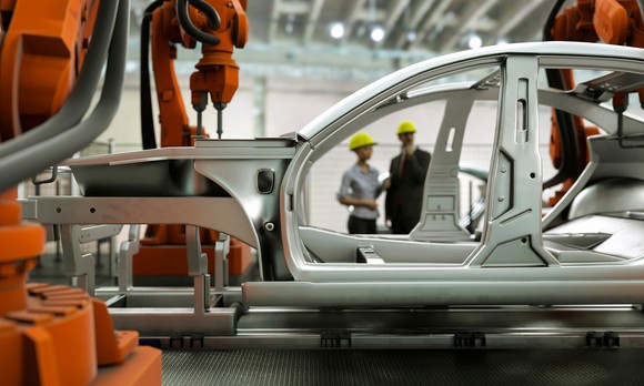 A car being produced by robot arms in a factory.