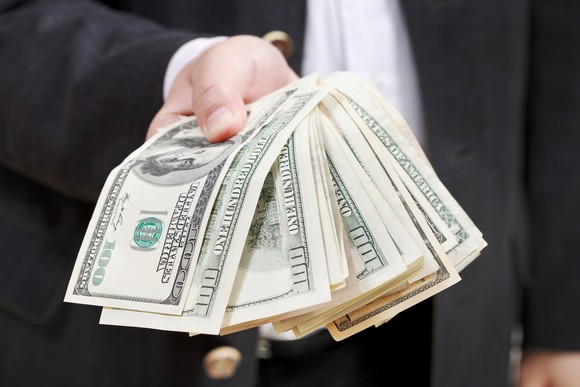 A hand holds out hundred-dollar bills.