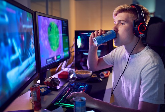 A gamer with a drink, looking at multiple screens.