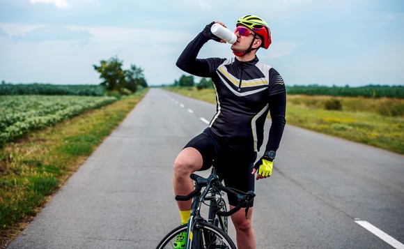 Cyclist stopped on road, drinking from bottle.