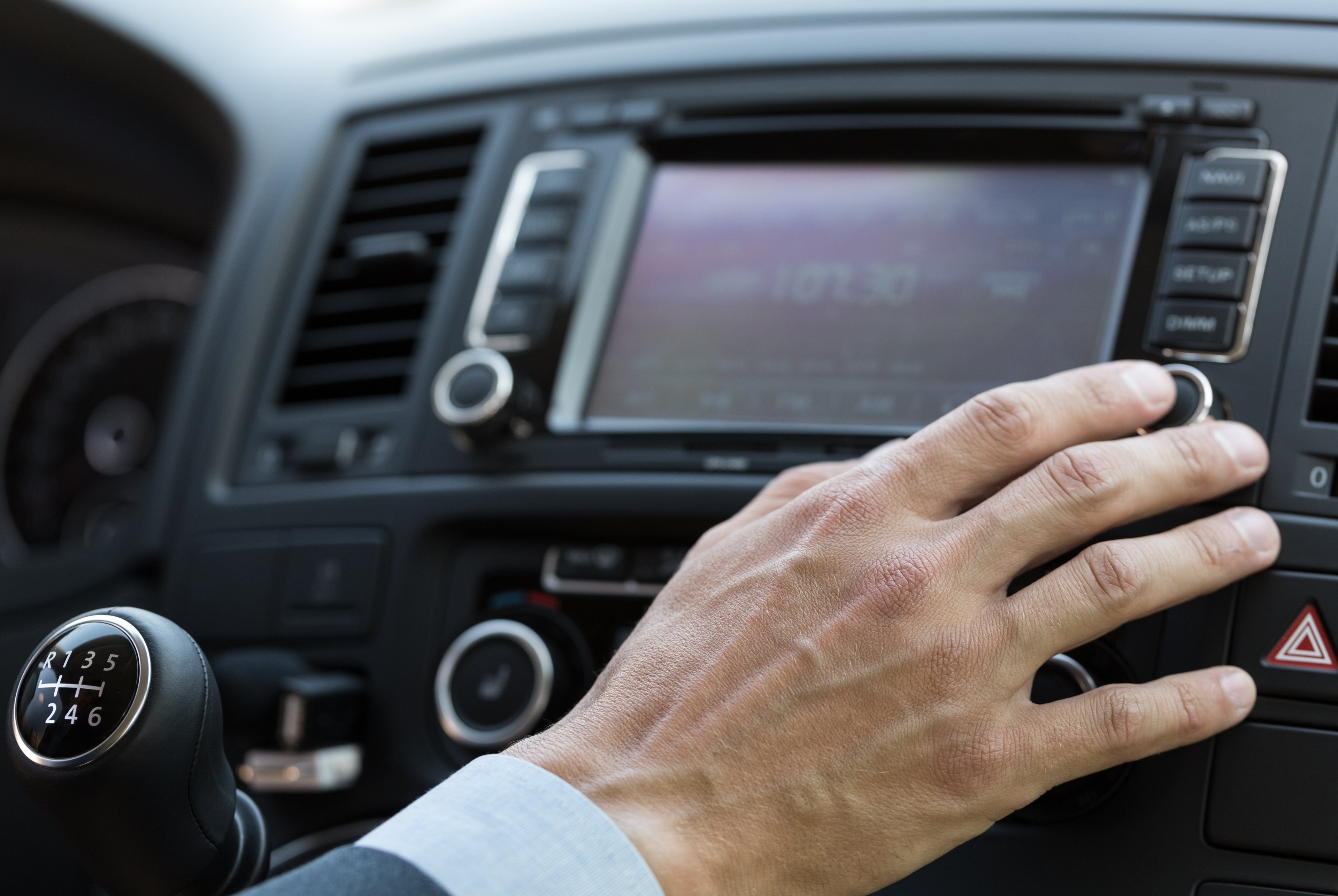 A man's hand works a car radio. 
