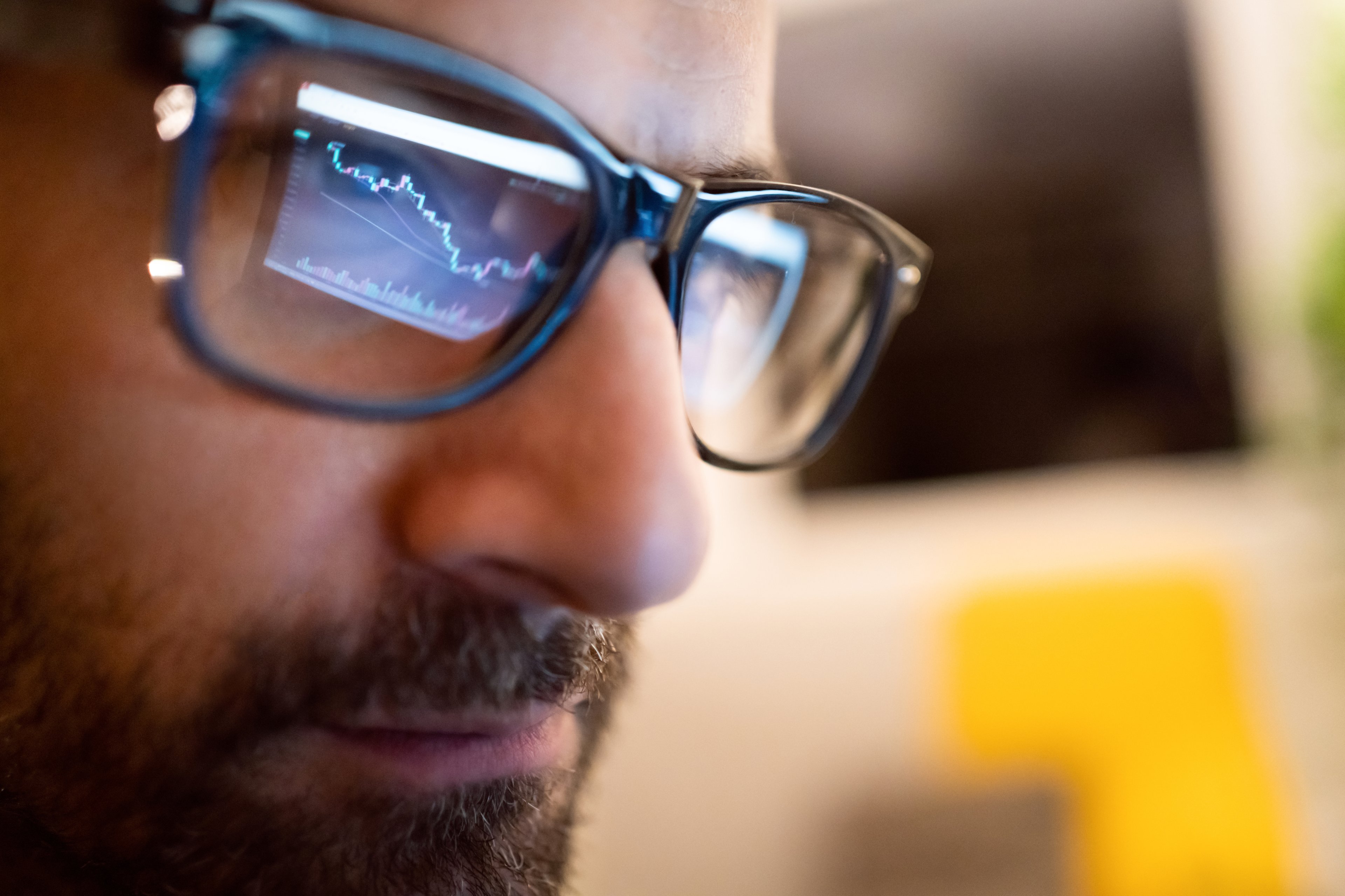 A person looking at a stock chart on a computer, as reflected in the viewer's eyeglasses.