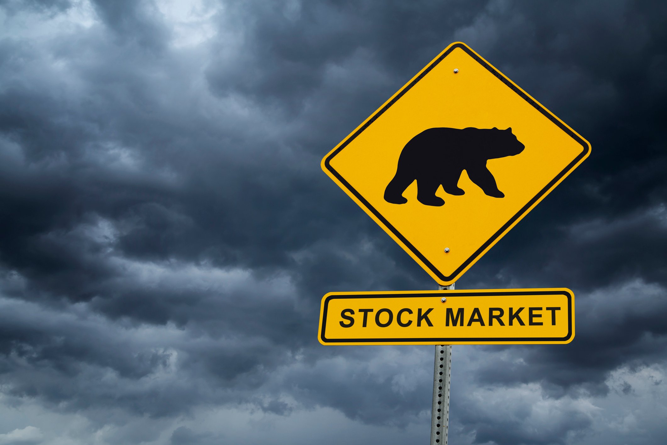 A silhouette of a bear on a road sign above a rectangular sign that reads "Stock Market" with dark clouds in the background.