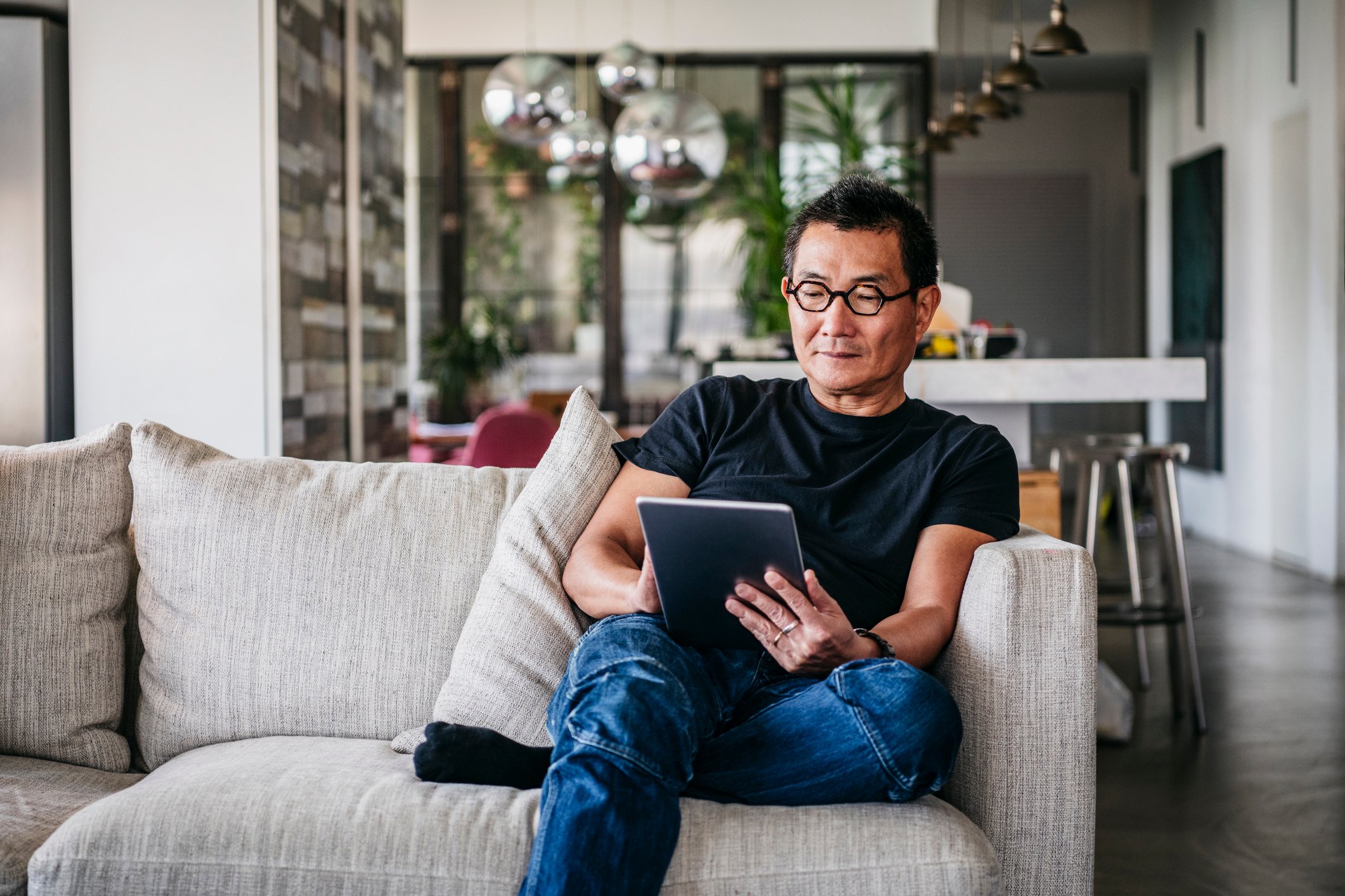 A man sitting on a couch looking at a tablet.